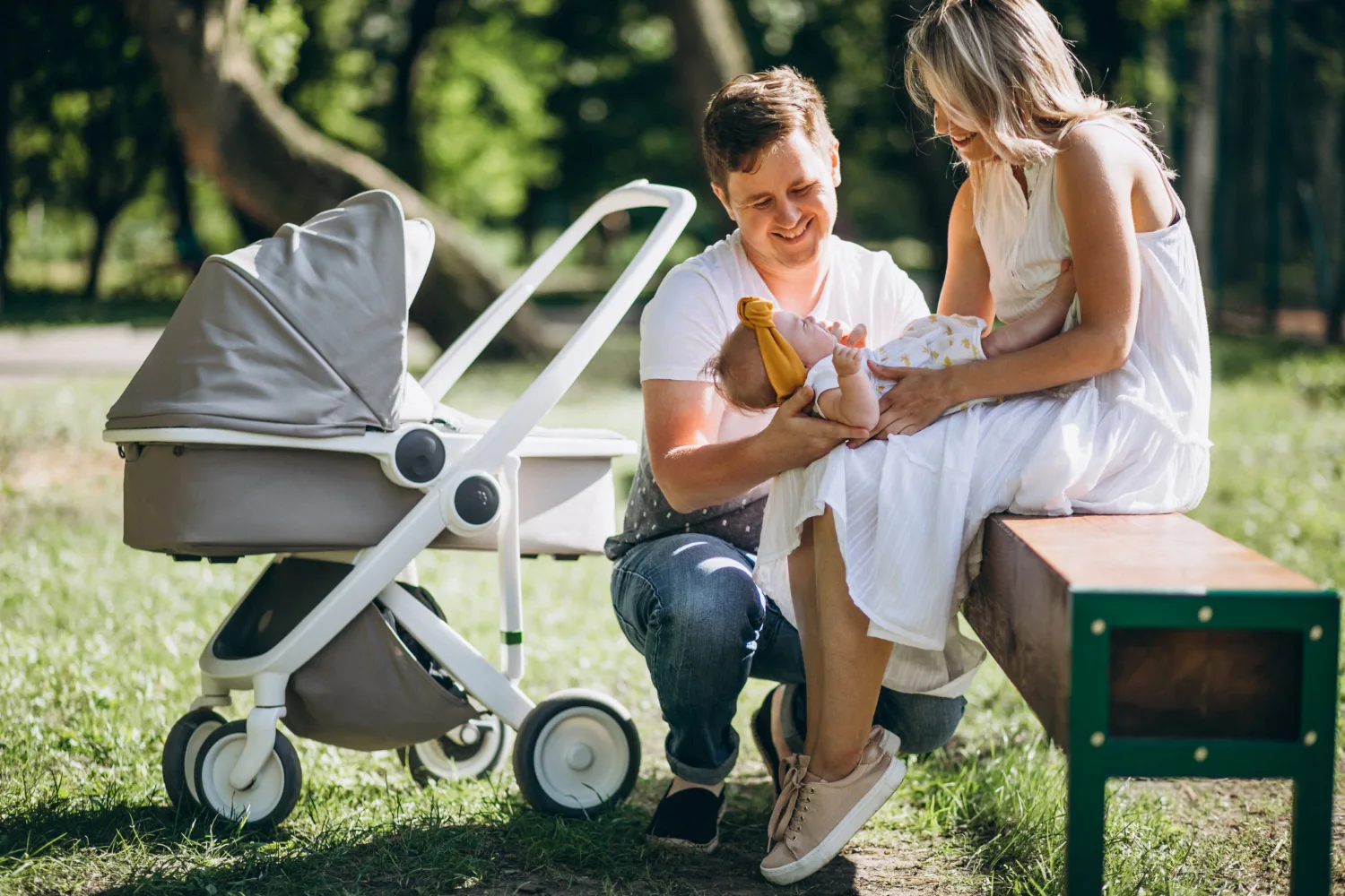 Des parents et leur bébé assis sur un banc, la poussette à côté
